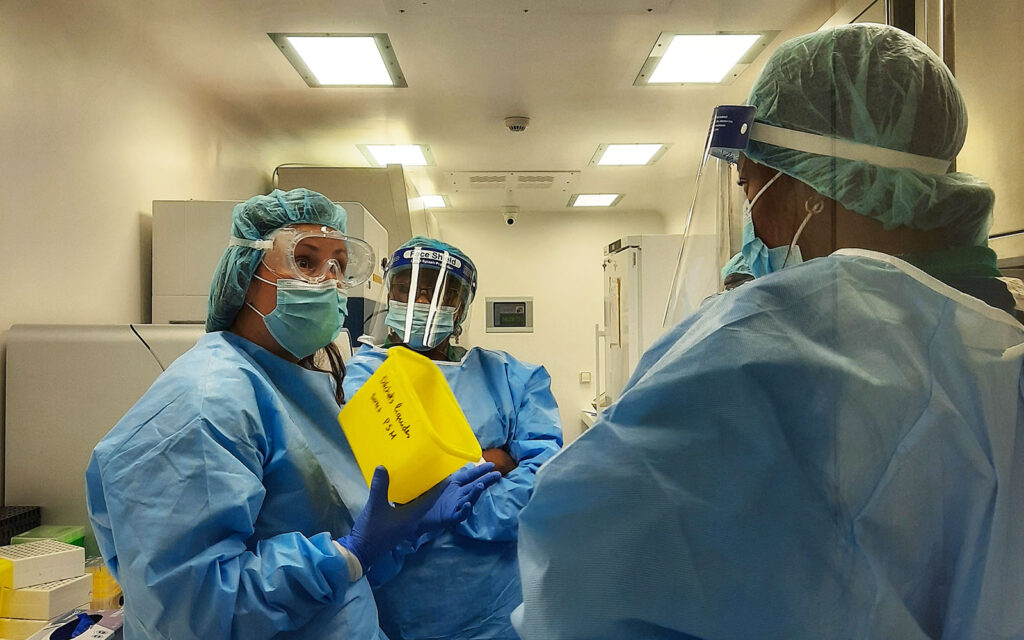 Three people in protective gear handling equipment in a laboratory in DRC