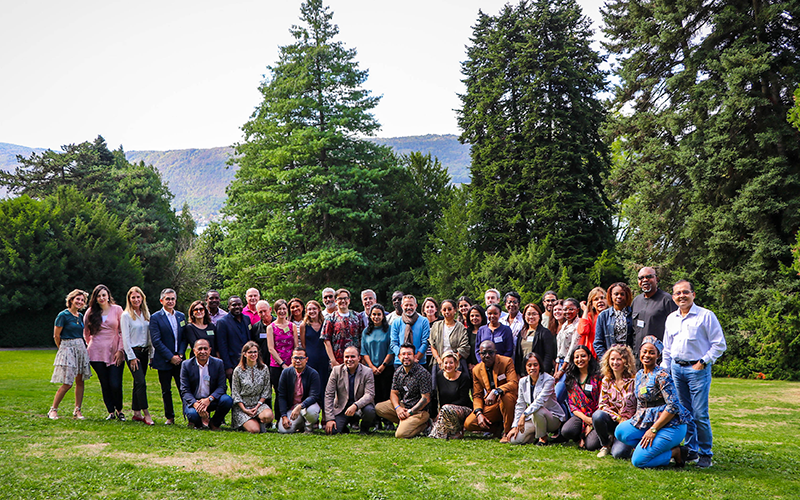 Group photo of participants in a park, trees in the background and Lake Annecy behind them.