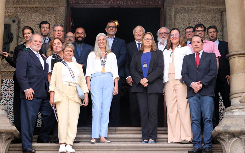 Photo de groupe des personnes présentes lors de la signature de l'accord, ils sont sur des marches. Il y a des colonnes à droite et à gauche, et à l'arrière, une porte