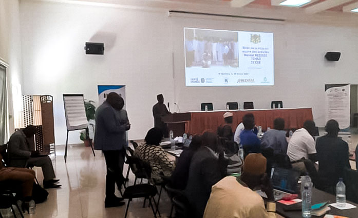 People are sitting on chairs, and there is a presentation projected on the wall.
