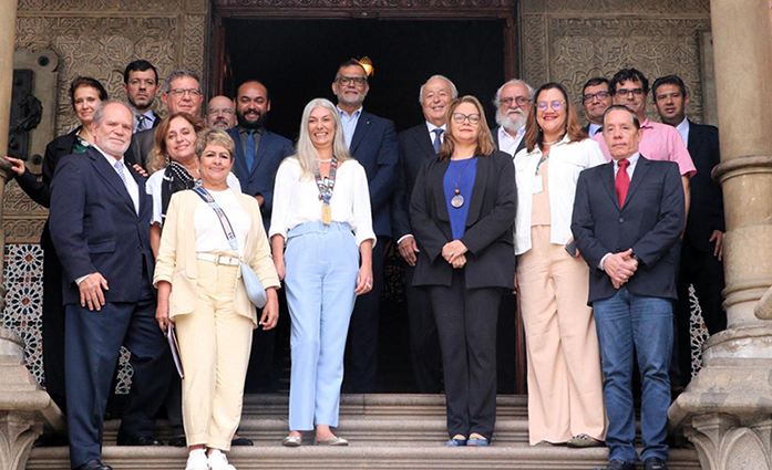 A group of people present at the signing of the agreement, they are on steps. There are columns on the right and left, and in the back, a door