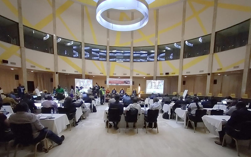 In a conference room, four people sit on a stage facing an audience seen from behind.