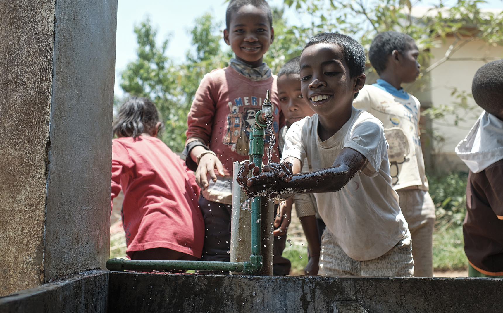 Malagasy children wash their hands in a basin outside, facing the view.