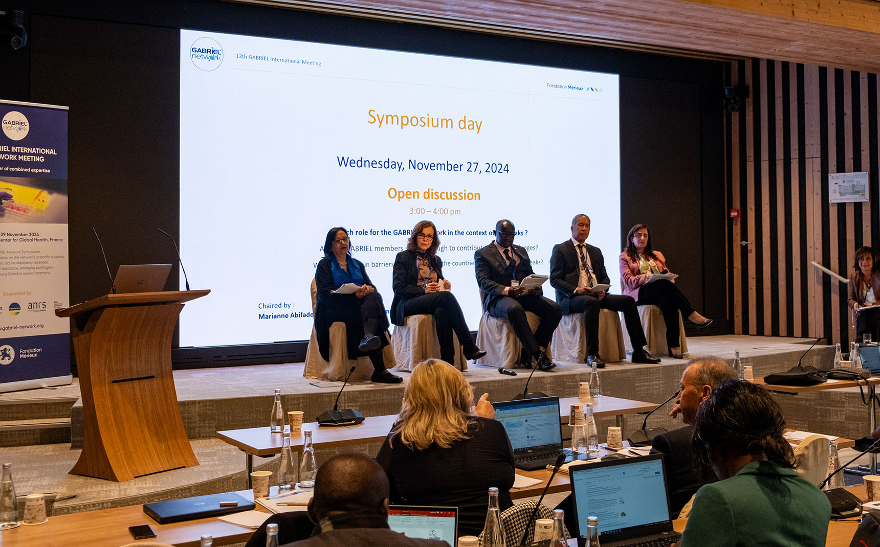 In a conference room, four people sit on the stage, facing the audience.