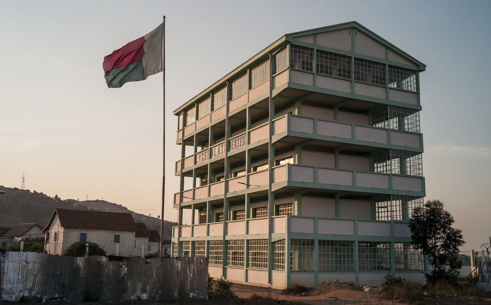 Outside, a view of a white and green building with the words Lycée Alain Mérieux written on it. To the left, a Madagascar flag.