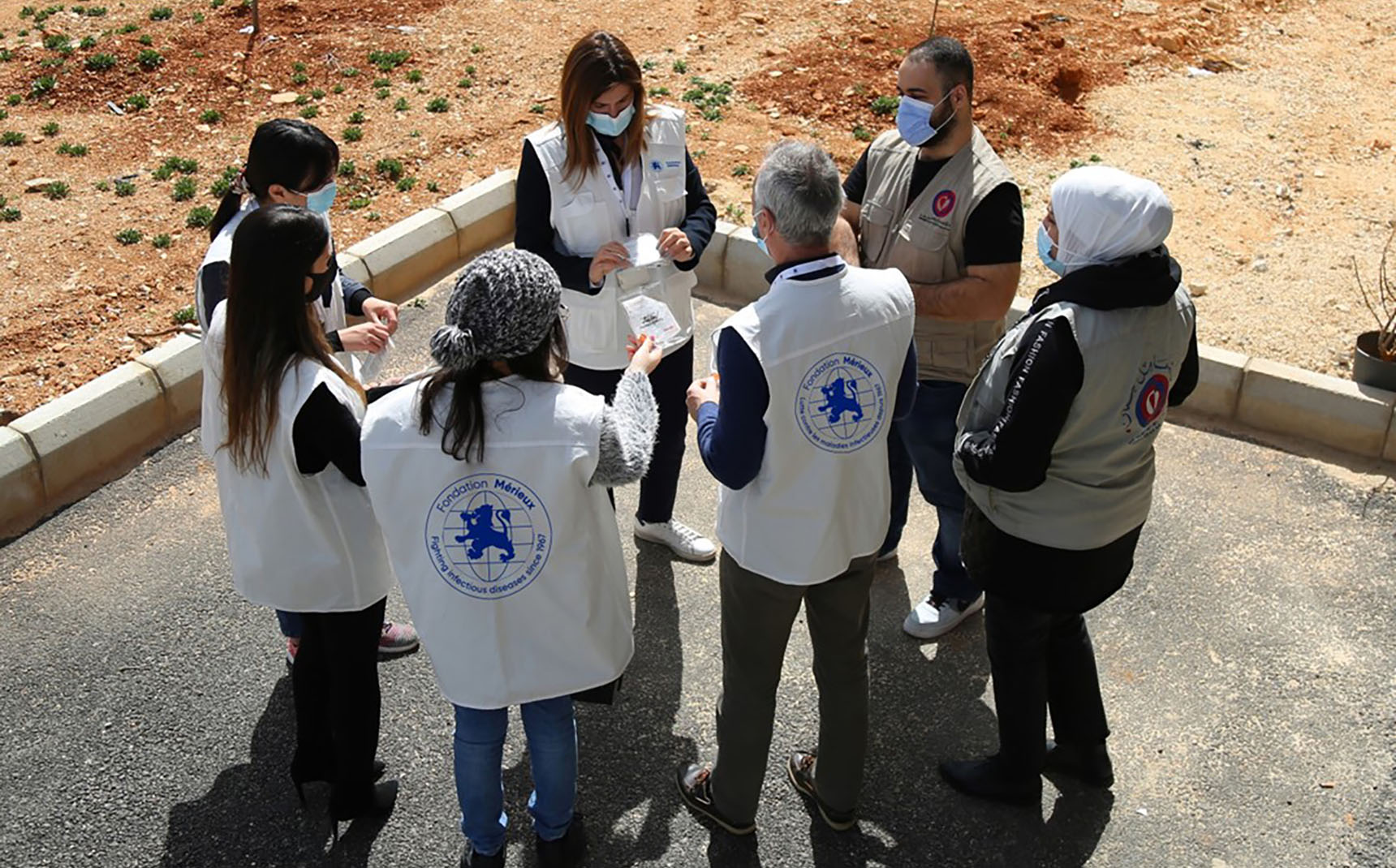 A group of people form a circle, wearing vests with the Mérieux Foundation logo.