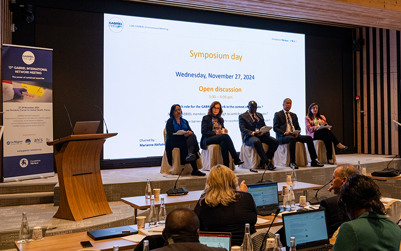 Five people sit on a stage in front of a large screen for an open discussion.