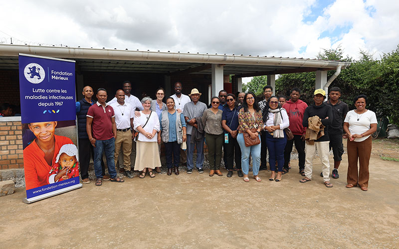 About twenty people are standing outside, in front of the canteen courtyard, with the Mérieux Foundation kakemono on their right.
