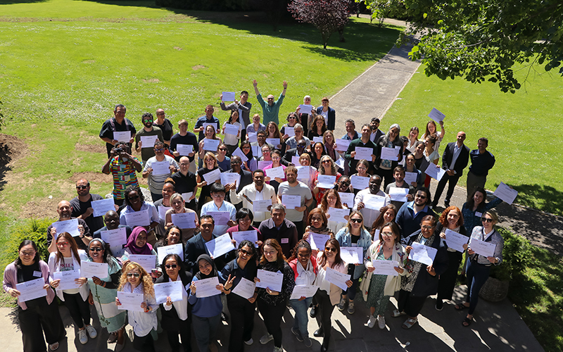 Low angle view of a group of people standing in the grass, holding paper diplomas in their hands.