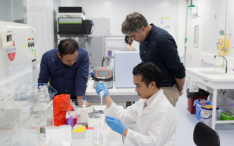 Three people in lab coats working with diagnostic equipment in a laboratory in Laos