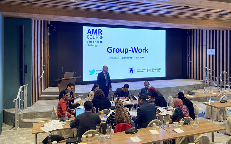AMR course participants gathered in a room for group work at Les Pensières Center for Global Health, with a screen displaying course information.