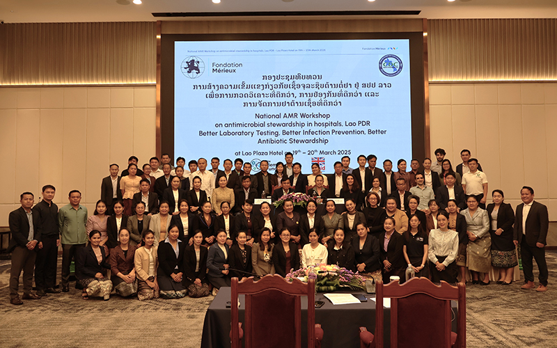 Conference room with a group of people posing, in the background a giant screen displays the name of the meeting in English and Lao.