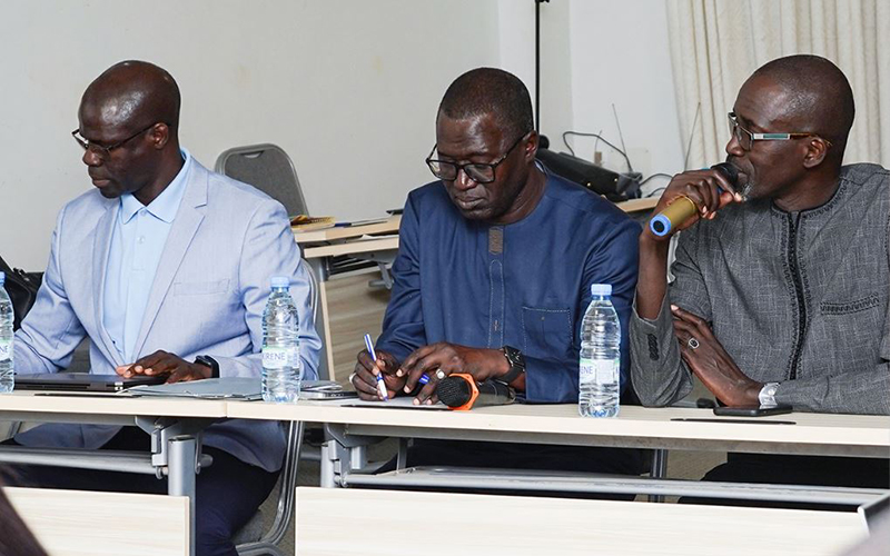 Salle de conférence avec trois participants assis de face avec une personne parlant au micro en s'adressant aux deux personnes à sa droite