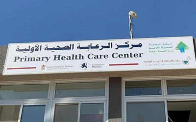 Haut d'une façade d'un batiment, grand panneau indiquant en anglais et en arable le nom du centre de santé de Rachaya suivi des logos des partenaires de soutien au projet