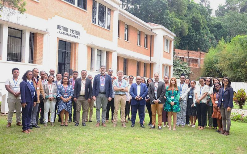 A group of people are standing in front of an orange and white building with the inscription ‘Institut Pasteur - Laboratories’.