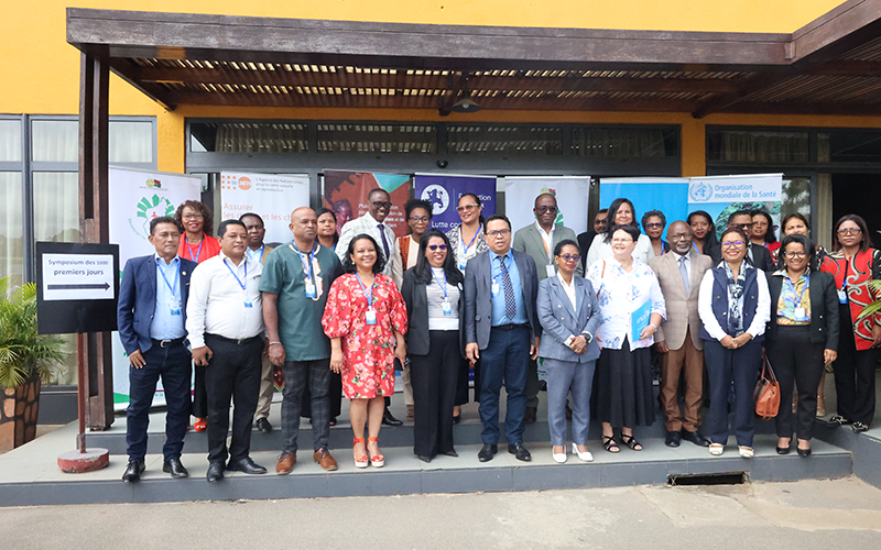 A group of people pose in front of a yellow building, under a wooden canopy. Behind the group, there are kakemonos.