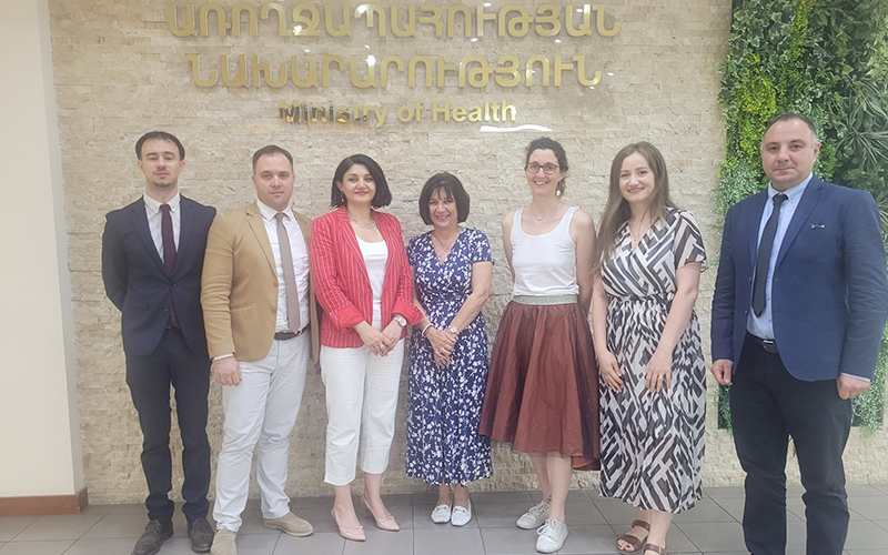 Group photo of 7 people in front of a wall with the words “Minister of Health” written on it